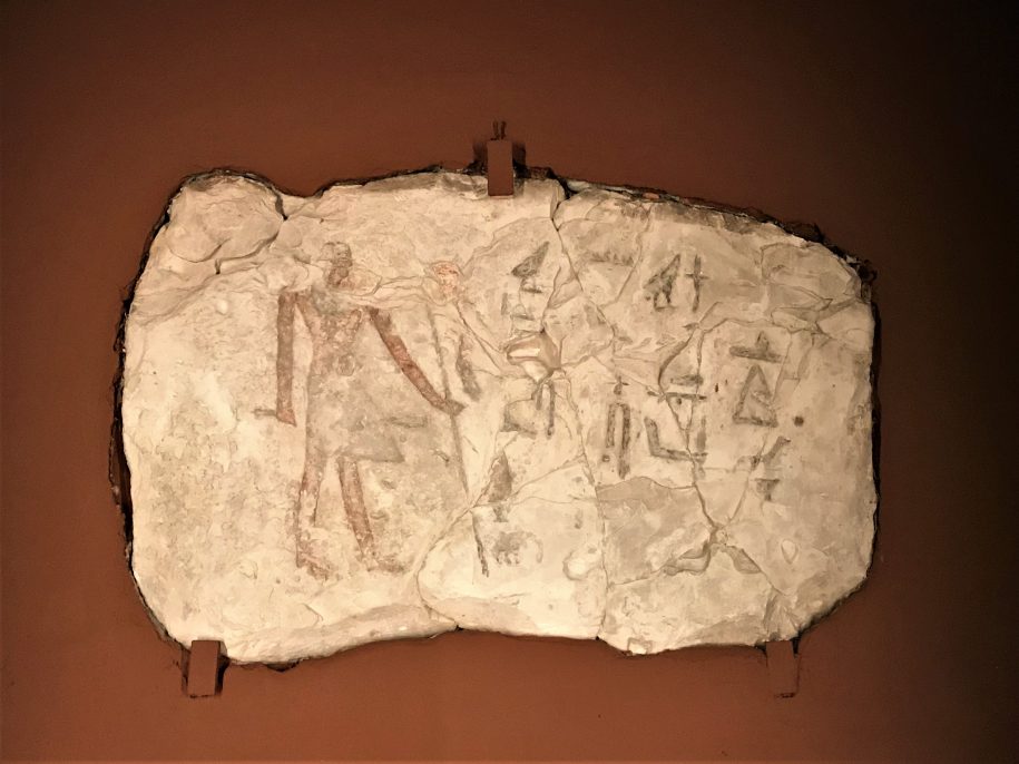 Kolorowe zdjęcie steli - białej, chropowatej, wykonanej z kamienia płyty grobowej ukazanej na brązowym tle.