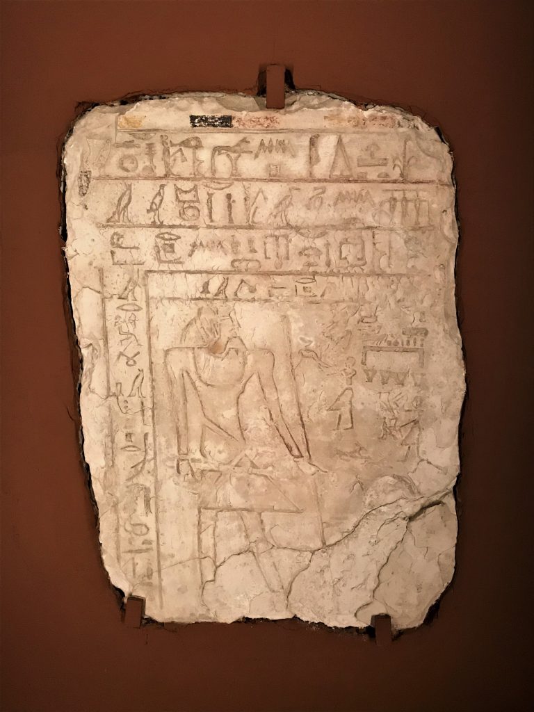Kolorowe zdjęcie steli - białej, chropowatej, wykonanej z kamienia płyty grobowej ukazanej na brązowym tle.